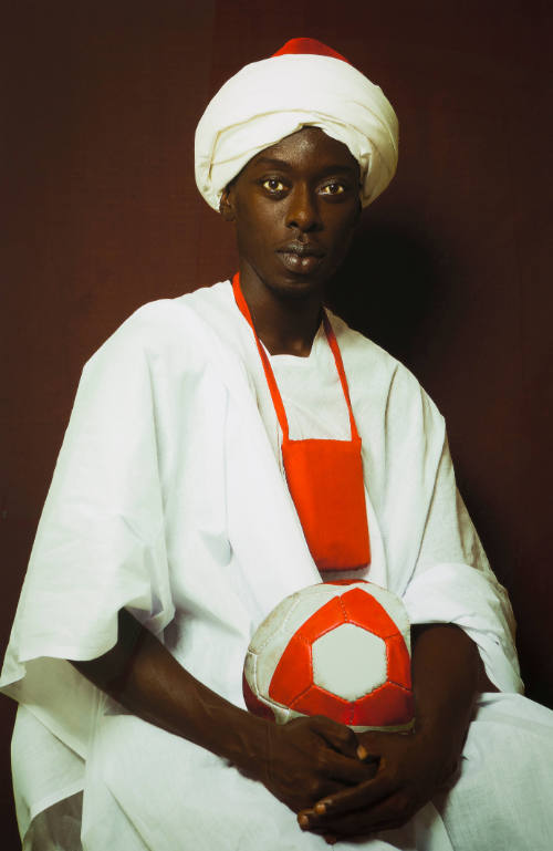 Portrait of man with dark skin tone dressed in a white robe and turban holding a ball on his lap