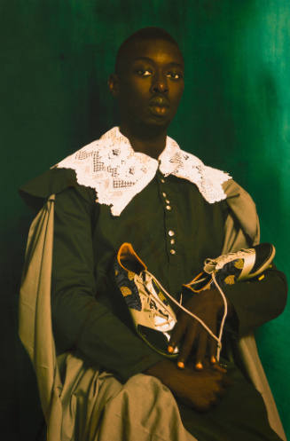 Portrait of dark-skinned man wearing dark green, a cape, and a lace collar, holding a pair of cleats