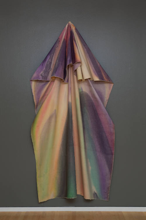 Unstretched, tie-dyed canvas hangs vertically from wall in an arrow-like shape