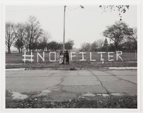 Four figures standing in front of a fence with water bottles in a pattern spelling "#NO FILTER"