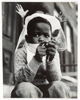 Black-and-white photo of child with dark skin tone wearing sweater, jeans, and bandanna around mouth