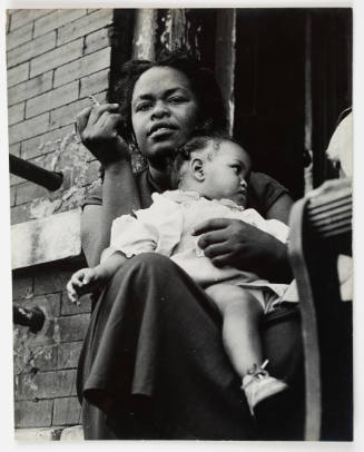 Black-and-white photo of seated adult with dark skin tone holding child and cigarette outside