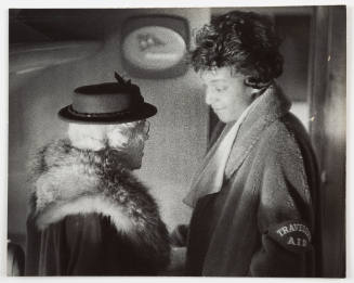 Black-and-white photo of two adults, one taller and younger, wearing coats and facing one other