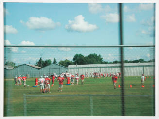 Blurry photograph of football players in red jerseys practicing on the field with blue sky above