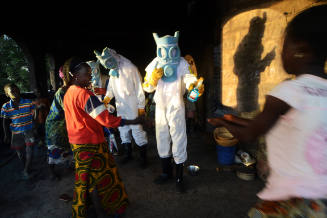 Three figures in personal protective equipment costumes holding spray bottles face four young people