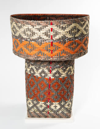 A cylindrical basket with white, brown, and orange paper woven in diamond pattern
