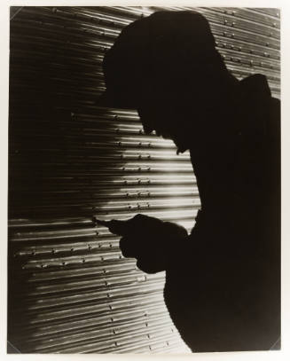 Silhouette of a person wearing a hat holding a tool up to a wall of corrugated metal