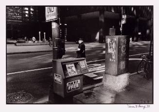 Black and white photo of street scene with newspaper box and person crossing street in center frame