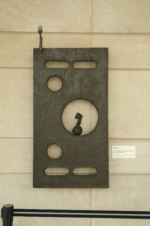 Rectangular bronze slab with circular holes and a fork sticking out the upper left-hand corner