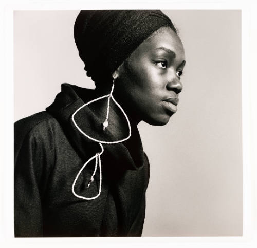 Black woman wearing black clothing, headwrap, and large dangling earring looks to the side