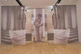 Gallery installation with transparent screens of photos, at center a Black woman dressed as goddess