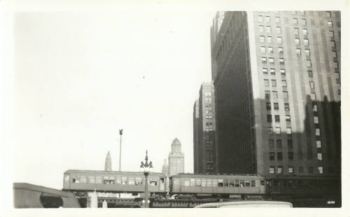 Black-and-white photograph of cityscape with moving train cars in the foreground and skyscrapers