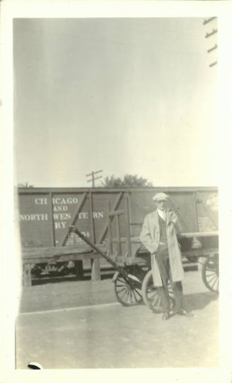 Black-and-white photo of a male-presenting person in front of a wood wagon and a railroad car
