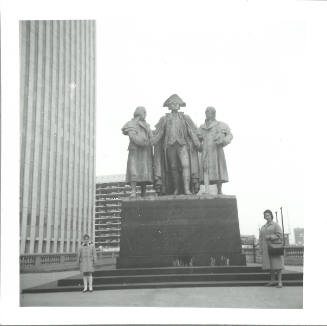 Black-and-white photograph of child and adult posing in front of Heald Square Monument in Chicago