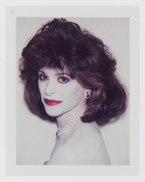 Polaroid of woman with dark feathered hair, white cakey makeup, red lipstick, and large jewelry