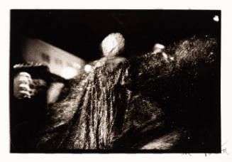 Blurry black-and-white photo of a person from behind, turning and wearing a sparkly, long coat 