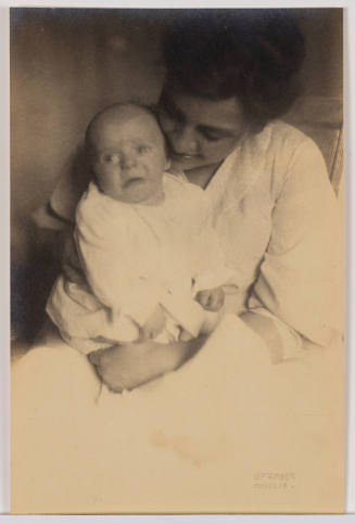 Sepia-tone photo of woman in white with light skin tone, tenderly looking down at the baby she holds
