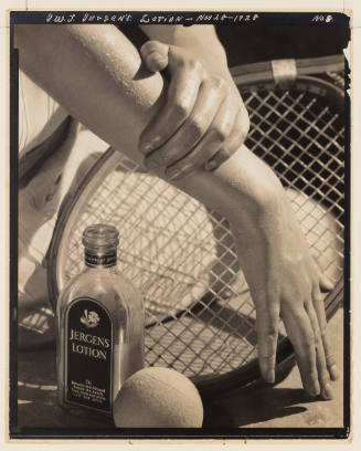 Black-and-white photo of light-skinned hands in front of a tennis racket with a bottle of lotion
