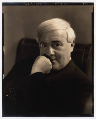 Portrait of a light-skinned man with white hair, posed with hand resting on his chin