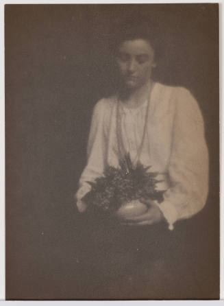 Woman in loose white shirt and long necklace looks down at vase in her hands
