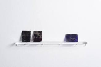 Three glass plates, each with a partial photo of the artist's face, on a clear shelf