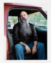 Man with a long gray beard is sitting with passenger door of red truck open