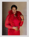 A female-presenting person with dark skin tone in a red dress and red feather boa