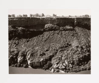 Black-and-white landscape photograph of an eroded deep canyon cliff with a small mound atop