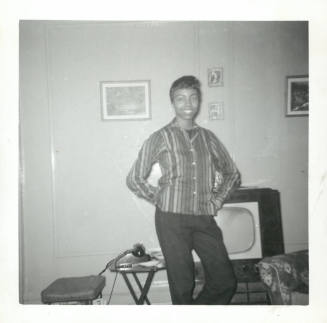 Smiling woman with dark skin tone wearing striped blouse standing in front of t.v. in living room