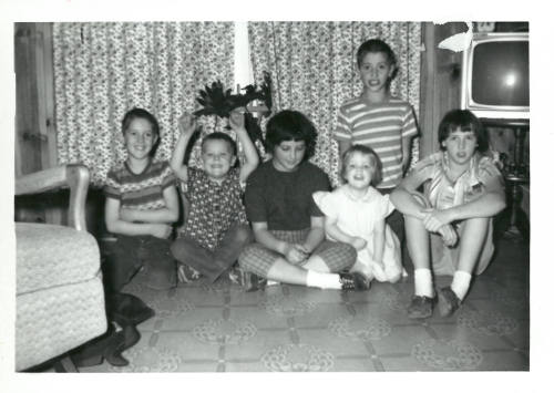 Black-and-white photo of six children sitting on the floor of a room with a television