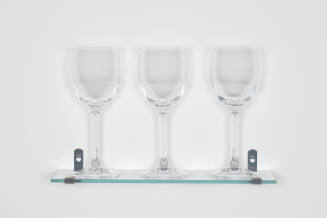 Three wine glasses on a glass shelf attached to a wall with metal brackets