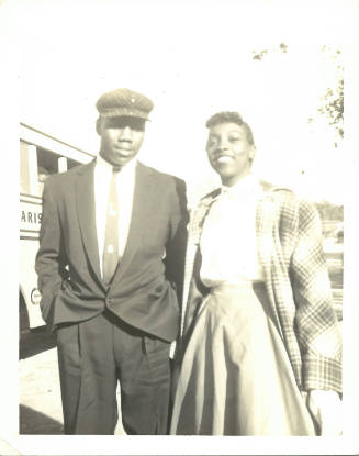 Man with dark skin tone in a suit and a woman with dark skin tone in a skirt and coat pose together