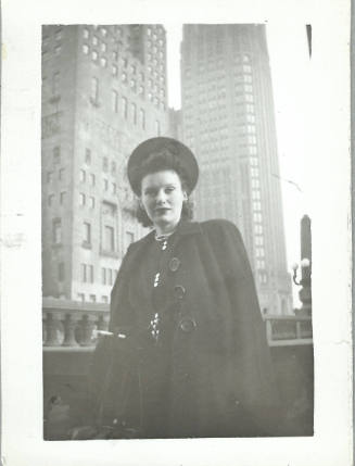 A white woman dressed in hat and coat with highrise buildings in the background