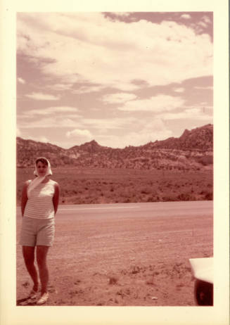 Photo with red tint of woman posing on side of the road with desert and cloudy sky in background