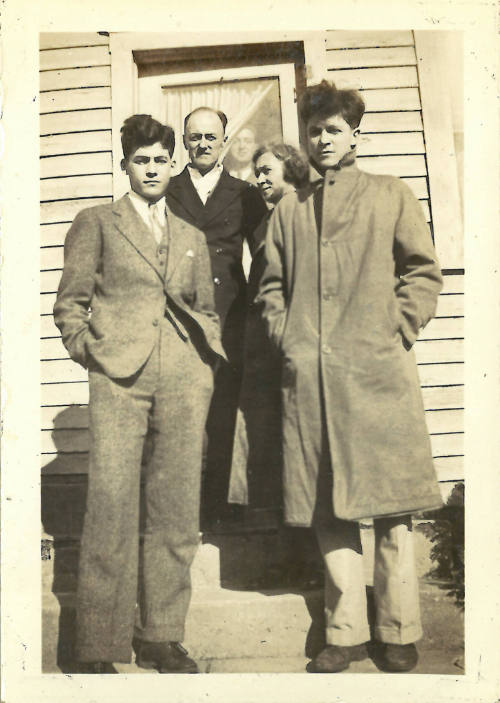 Four people with light skin tone look into camera, another looks through from behind the door