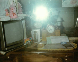 Color photo of dresser with clock, TV, postcards and other items on top, and mirror in background