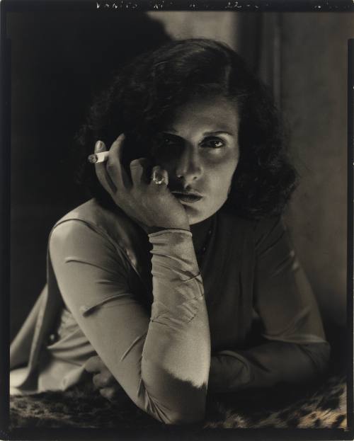 Black-and-white photograph of a light-skinned woman leaning forward and holding a cigarette 