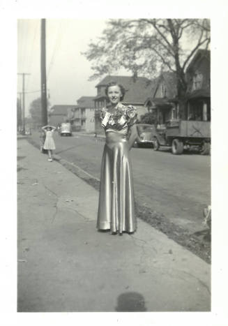 Smiling young woman with light skin tone on sidewalk wearing long, formal satin dress