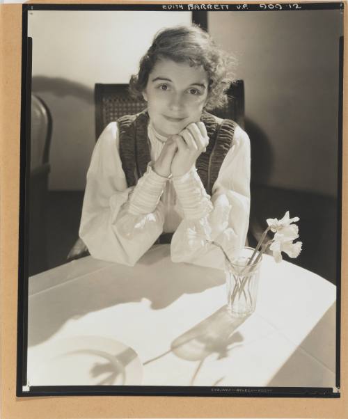 Photo of smiling woman with light skin tone and dark hair seen from across dining table with flowers
