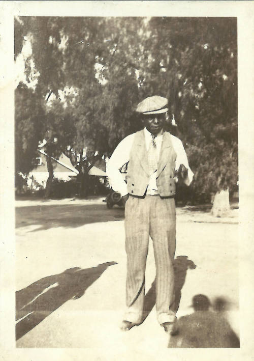 Man with dark skin tone wearing formal clothing outdoors with shadows of three people in foreground