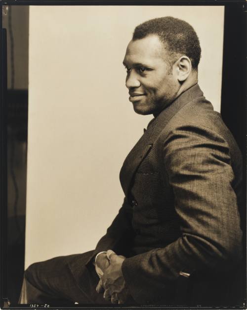 Side profile of a Black man wearing a suit as he smiles and poses his body toward the left