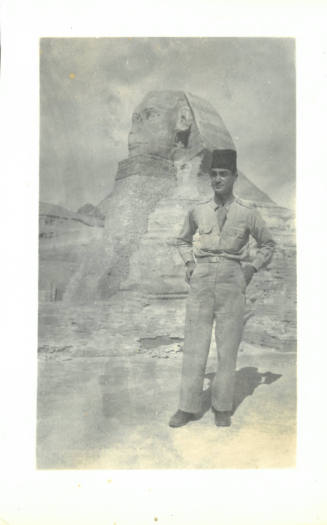 Man wearing shirt, tie, trousers and fez stands facing forward, with Egypt's Great Sphinx behind