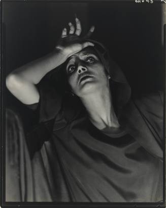 Dramatically lit black-and-white photograph of a woman leaning back with one hand to her forehead