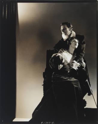 Theatrical black-and-white photo of man and woman with light skin tone, in costumes and embracing 