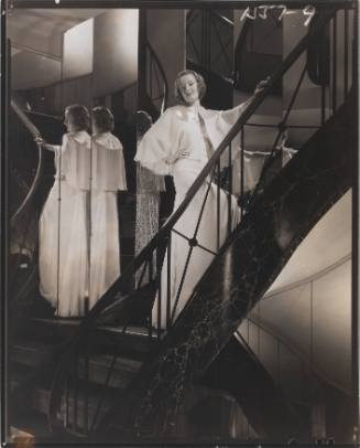 Fashion photo of a woman on a staircase in a white floor-length dress, reflected in mirrors