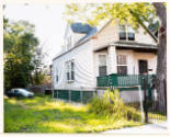 A two-story white clapboard house with dark green trim; the lot adjacent is vacant