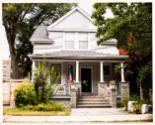 A two-story light gray clapboard house; and American flag displayed on the porch