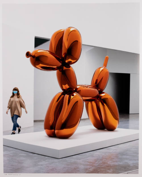 Photograph of museum visitor in sanitary mask walking behind a large sculpture of a balloon animal