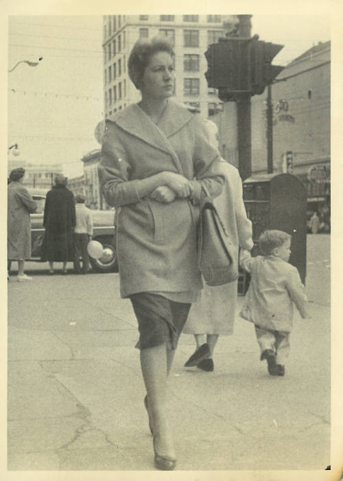 Woman with light skin tone in lapel coat and heels walking down a crowded street