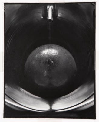 Black-and-white close-up photograph of a metal orb at center, enveloped by circular streams of light